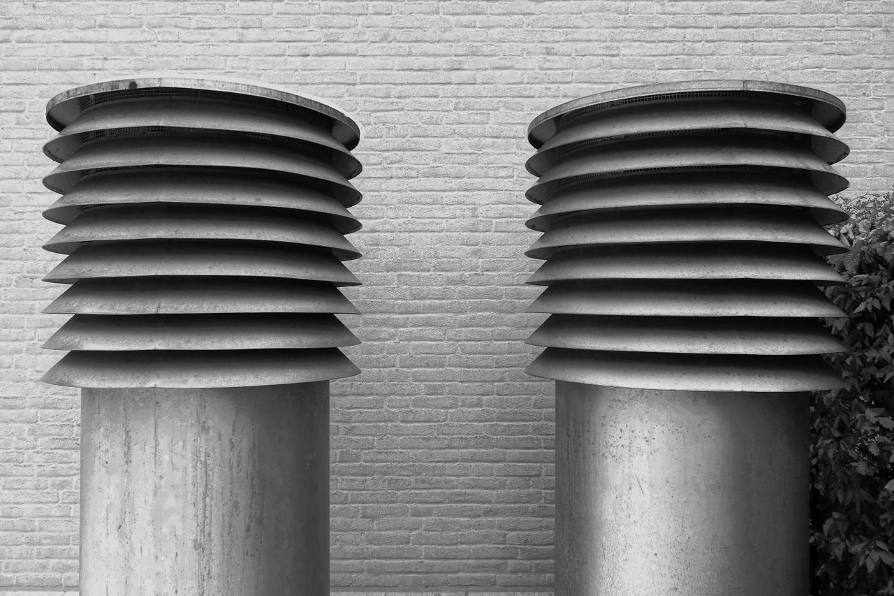 Black and white photo of two industrial ventilation pipes with a brick wall background and minimalist design.