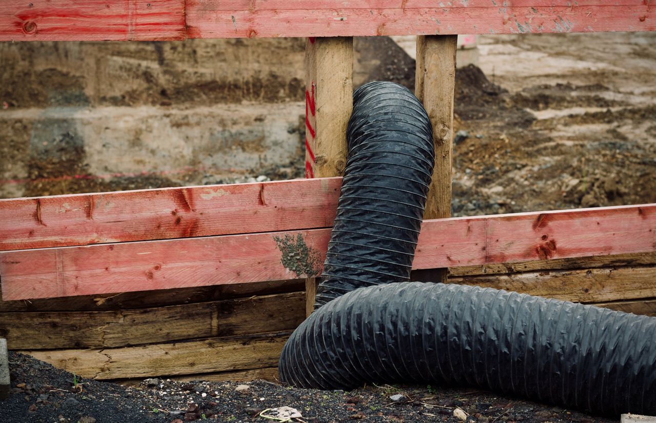 Close-up of a construction site showing red wooden barriers and a flexible black duct.